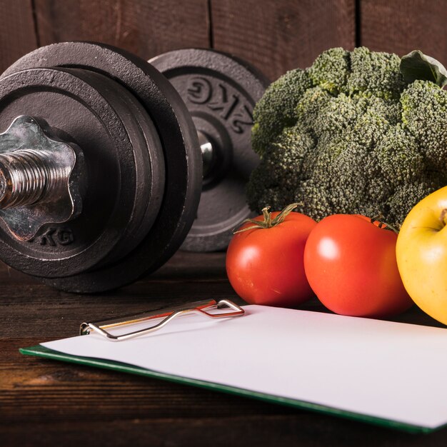Close-up of healthy raw food and dumbbell on wooden desk
