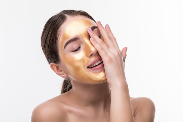 柔らかい肌にゴールドの化粧フェイスマスクを持つ健康な若い女性のクローズアップ。