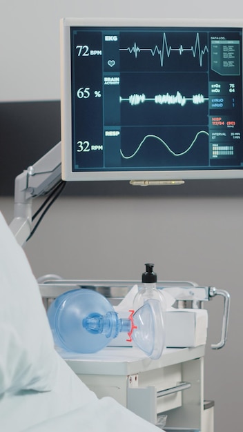 Close up of heart rate monitor in empty hospital ward. Nobody in intensive care room with medical equipment, bed, oxygen tube and wheelchair for recovery. Healthcare instruments