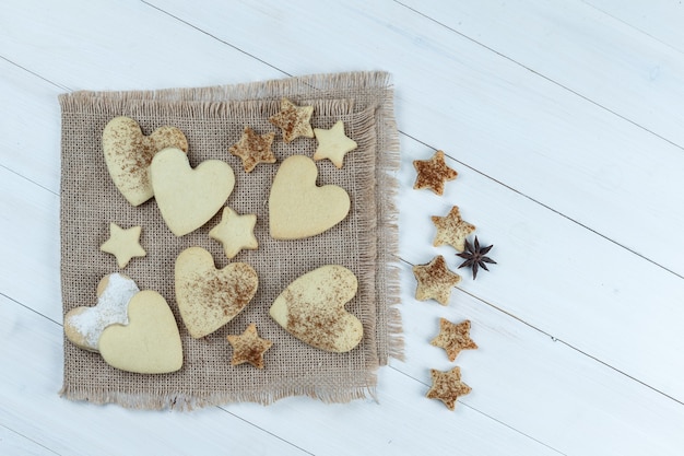 Close-up heart-shaped and star cookies on piece of sack with star cookies on white wooden board background. horizontal
