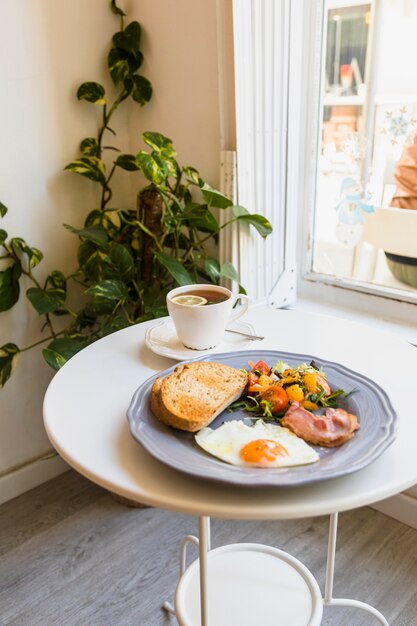 Close-up of herbal tea; freshly cooked eggs; salad; bacon and toast on plate over the table