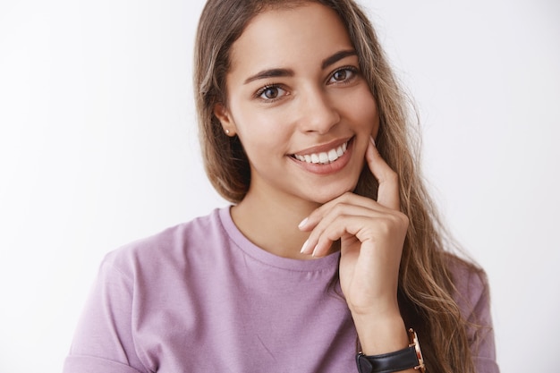 Close-up hispanic cute tender woman 25s tilting head flirty smiling giggling joyfully, feeling happy, touching cheek finger, taking care skin, fighting facial scars, delight skincare products result