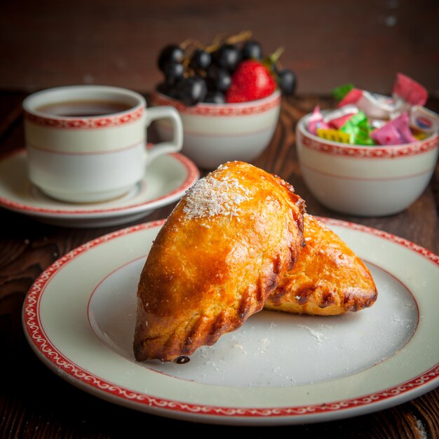 Close-up homemade bakery with cup of tea, candies and berries on wooden table