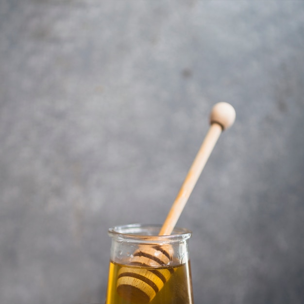 Close-up of honey dipper in the honey pot over the grey backdrop