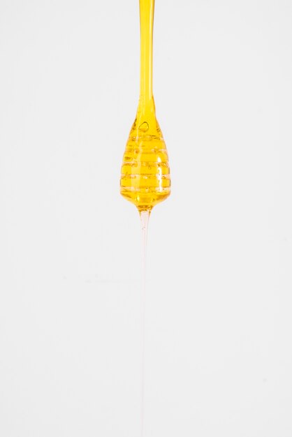 Close-up of honey dripping from dipper on white background