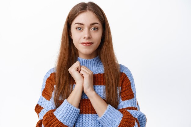 Close up of hopeful cute girl student, hold hands near chest and smiling at camera with grateful face expression, express gratitude or admiration, white background