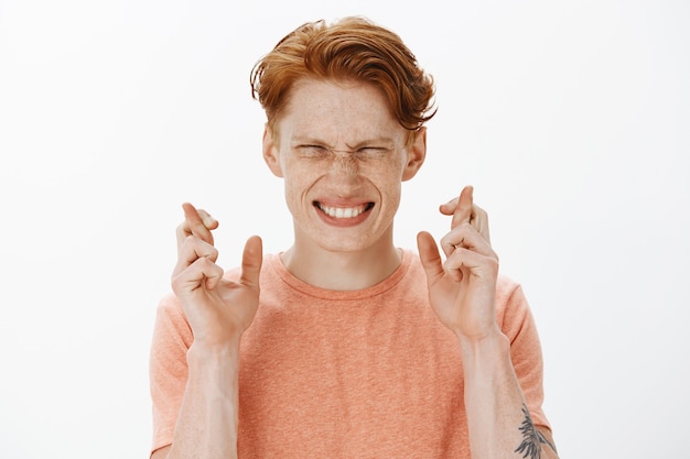 Free photo close-up of hopeful redhead man student cross fingers good luck, making wish