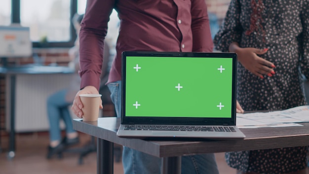 Close up of horizontal green screen on laptop at office. Pregnant woman and man having chroma key with isolated background and mockup template on computer. Business people with technology at work