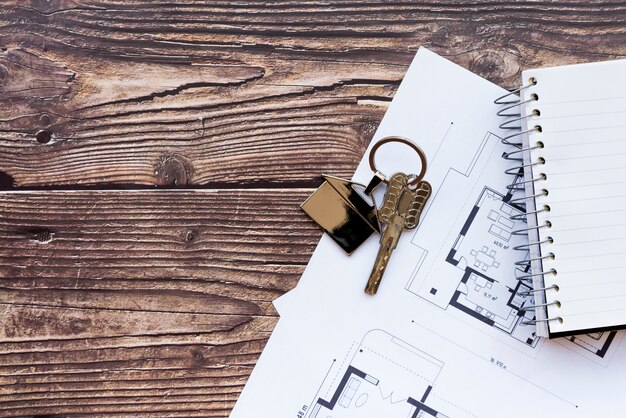 Close-up of house keys on blueprint of new home and spiral notebook on wooden textured backdrop