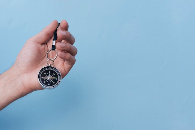 Close-up of human hand holding navigational compass on blue backdrop