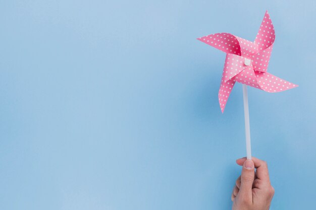 Close-up of human hand holding polka dotted pinwheel on blue backdrop