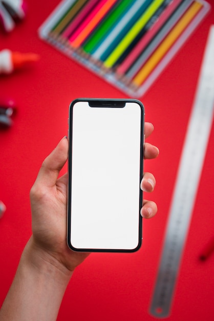 Close-up of a human hand holding smartphone with blank white display over blurry backdrop