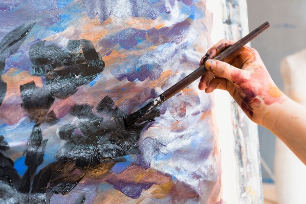 Close-up of human hand painting on canvas with paintbrush