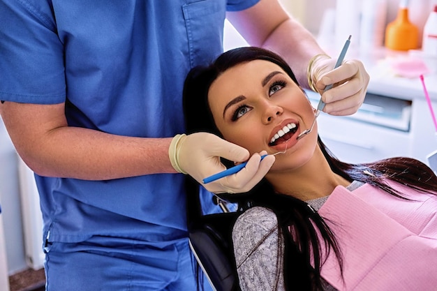 Крупный план стоматолога, осматривающего женские зубы в стоматологии.