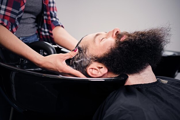 サロンで散髪する前にひげを生やした男性の髪を洗う女性の美容師の画像をクローズアップ。