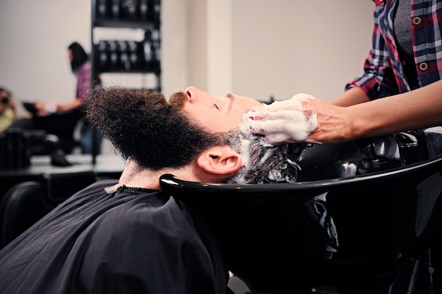 Close up image of female hairdresser washing bearded men's hair before haircut in a saloon.