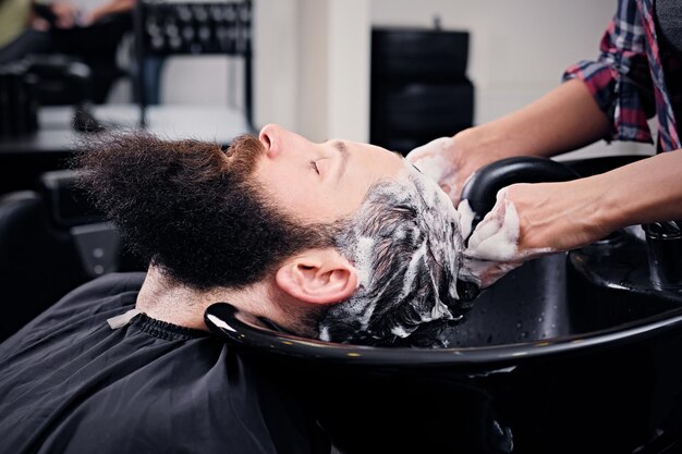 サロンで散髪する前にひげを生やした男性の髪を洗う女性の美容師の画像をクローズアップ。