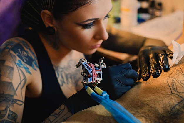 女性のタトゥーアーティストのクローズアップ画像は、男性の胴体にタトゥーを入れます。
