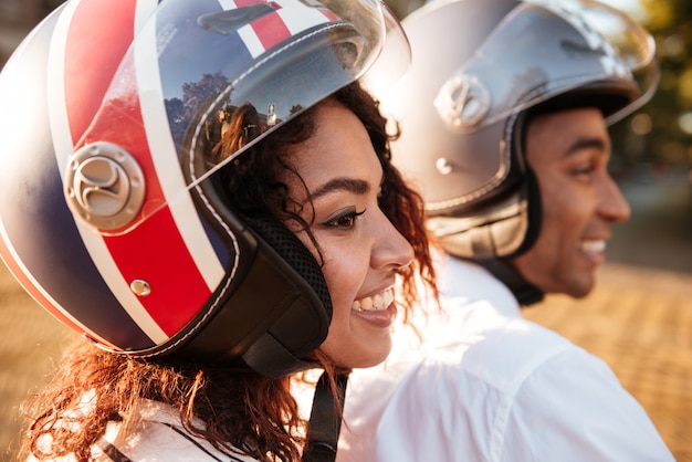 Close up image of pleased african couple rides on modern motorbike on the street