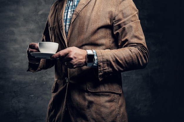 Close up image of redhead bearded male holds a cup of coffee over grey background.