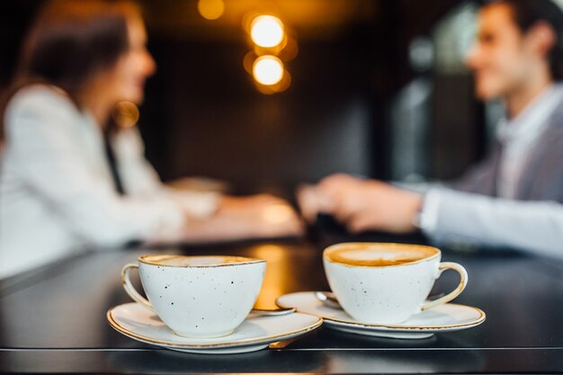 カフェの木製テーブルにラテと2つのコーヒーカップの画像を閉じます。