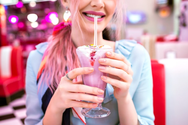 Close up image of woman holding sweet strawberry milk shake, pin up retro style, pastel colors, vintage American cafe