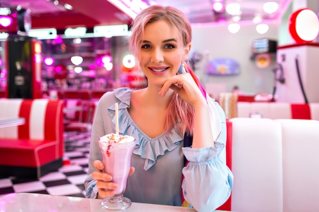 Close up image of woman holding sweet strawberry milk shake, pin up retro style, pastel colors, vintage American cafe.