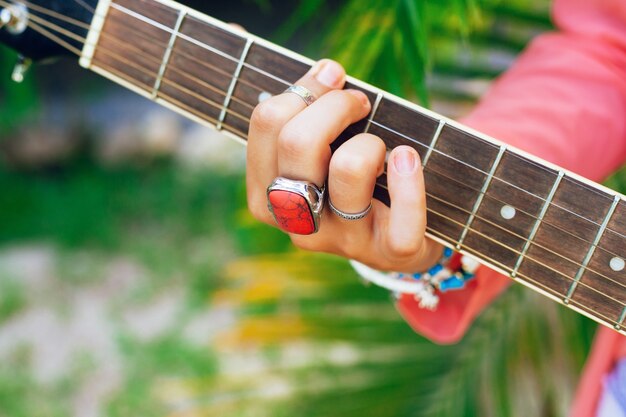 Close up image of woman playing on acoustic guitar, bright accessorizes, green palms background.