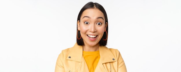 Close up of impressed asian girl say wow looking amazed at camera standing in casual clothes over white background