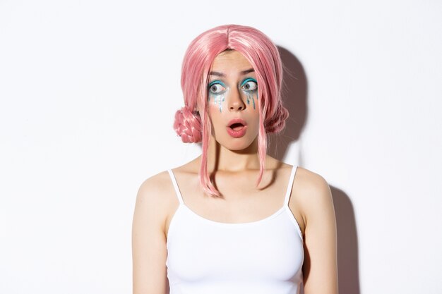 Close-up of impressed attractive girl in pink wig, open mouth in awe and looking left, standing.