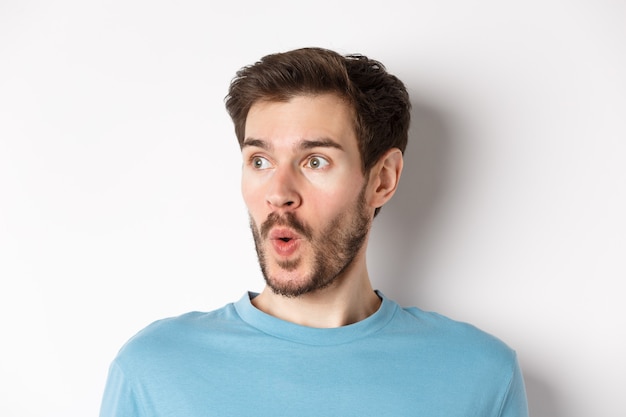 Close-up of impressed caucasian man saying wow, looking left amazed, checking out promotion deal, white background. Copy space