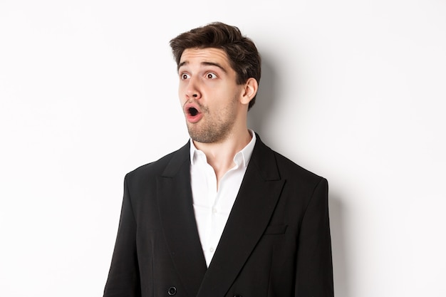 Close-up of impressed guy in trendy suit, open mouth and looking left wondered, standing against white background