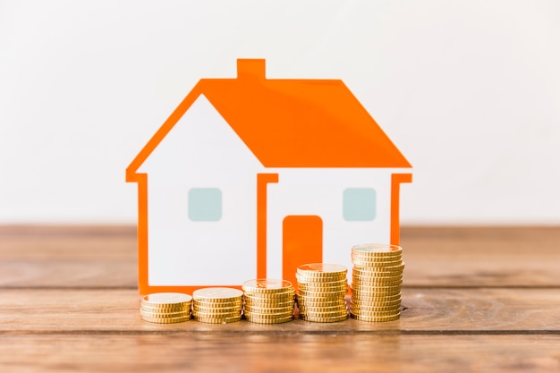 Close-up of increasing stacked coins and house model on wooden desk