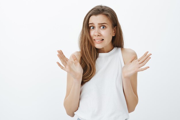 Close-up of indecisive worried girl shrugging and raise hands up with confused grimace