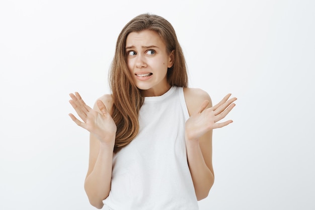 Close-up of indecisive worried girl shrugging and raise hands up with grimace