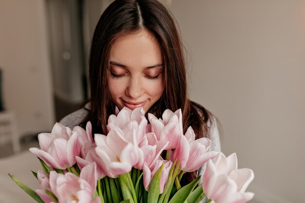 目を閉じてポーズをとって黒い髪と花を持って幸せな笑顔で幸せな女の屋内ポートレートを閉じます。