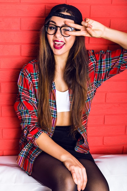 Close up indoor ritratto di giovane bella ragazza hipster con lunghi capelli castani e trucco luminoso, mostrando yo scienza e ridendo,