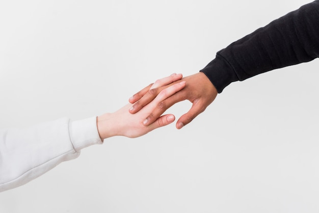 異人種間のカップルが白い背景に対して互いの手を握ってのクローズアップ