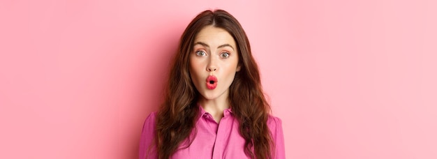 Close up of intrigued young woman gasping saying wow and looking impressed at camera standing over p