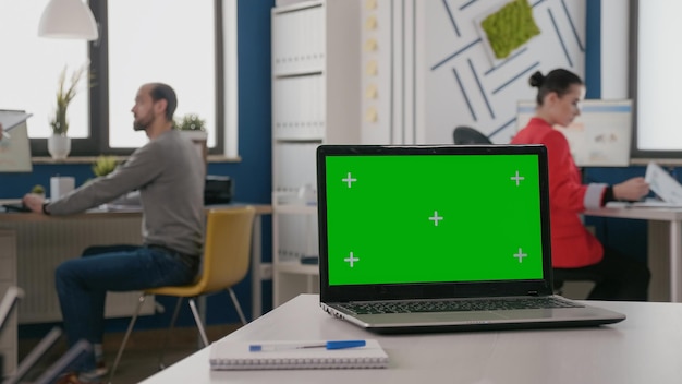 Закройте изолированный зеленый экран на ноутбуке за пустым столом. Устройство с макетом шаблона и фоном хроматического ключа на дисплее. Компьютер с хромакеем и приложением-макетом на экране.