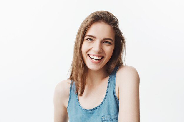 Close up isolated portrait of charming cheerful young caucasian young woman with dark hair and brown eyes smiling showing teeth,  with relaxed and happy expression. Positive emotions