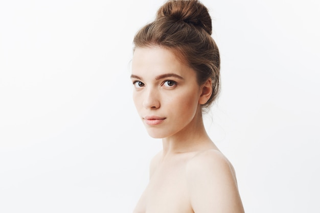Free photo close up isolated portrait of relaxed beautiful young skinny woman with long dark hair in bun hairstyle, posing half naked in three quarters with calm expression.