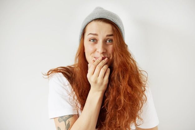 Close up isolated portrait of young redhead woman laughing, covering mouth with her hand