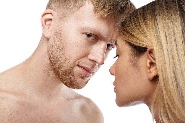 Close up isolated view of attractive shirtless unshaven Caucasian guy going to make love to beautiful tender blonde woman. Adult couple posing naked, hugging and kissing. Sex and sensuality