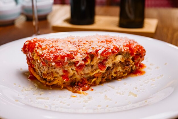 Close up of italian lasagne garnished with tomato sauce and grated parmesan