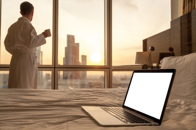 Free photo close-up of laptop on the bed with man in bathrobe background