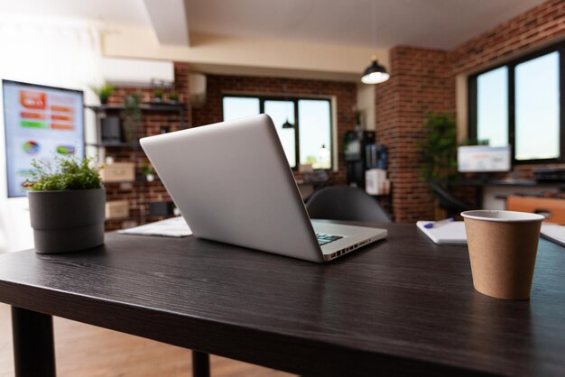 Close up of laptop and office supplies on wooden desk. Nobody in empty business space with computer, cup of coffee and equipment used to work on startup company in boardroom. Modern decor