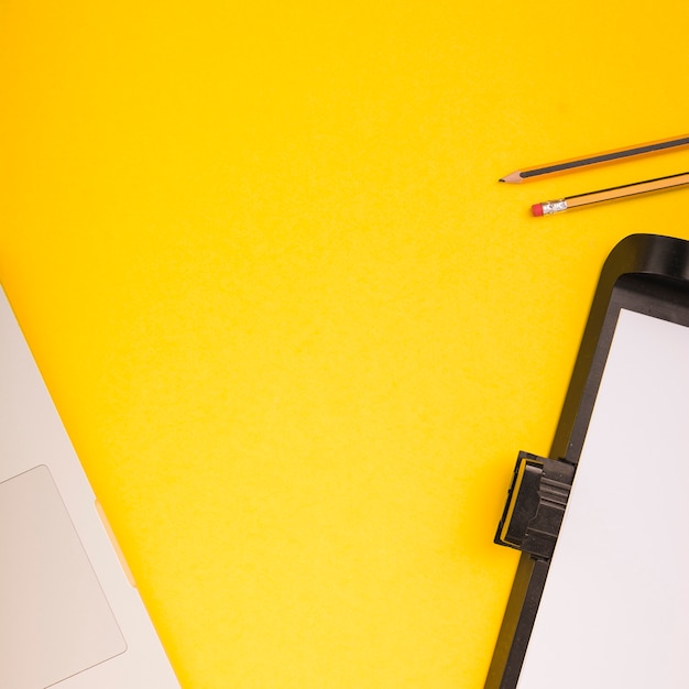 Close-up of laptop; pencils and printer tray with blank paper on yellow background