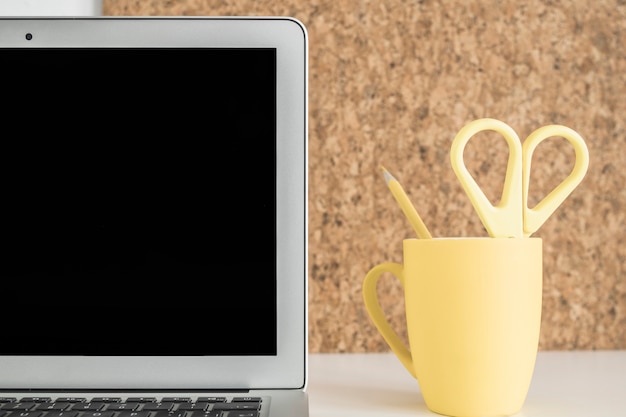 Close-up of laptop screen with scissor and pencil in yellow cup on desk