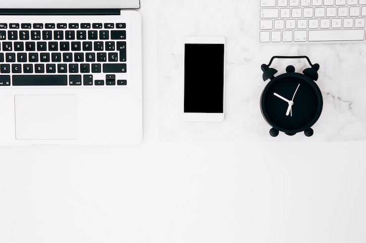 Free Photo close-up of laptop; smartphone; alarm clock and keyboard on white texture desk